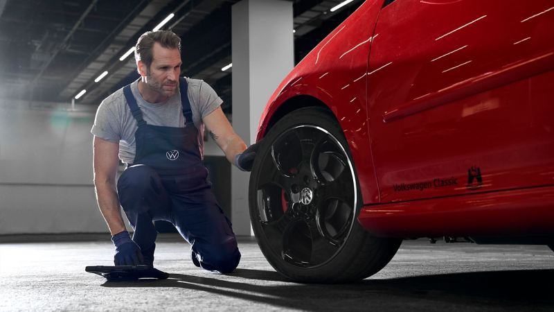 A VW service employee takes a look at the car tyre of a red VW – wheel knowledge