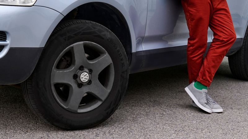 Vista detallada de un neumático de un Touareg 1, junto a él un hombre con pantalones rojos - Accesorios Volkswagen 