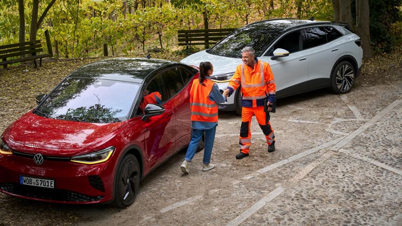 Woman with safety vest and Volkswagen Roadside Assistance employee next to two VW ID. cars