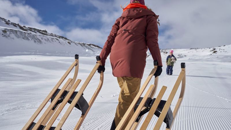 Eine Frau trägt zwei Schlitten den verschneiten Berg hoch