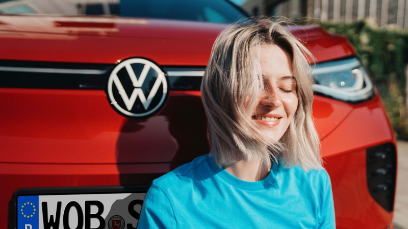 Eine zufriedene Frau sitzt vor einem roten VW ID.4 GTX