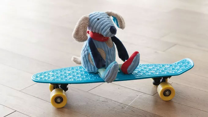 La peluche "Mick Mechanic" de la collection enfant VW est assise sur un skateboard.