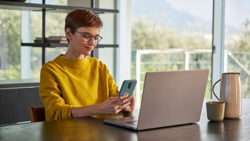 Frau mit Smartphone in der Hand schaut auf Laptop