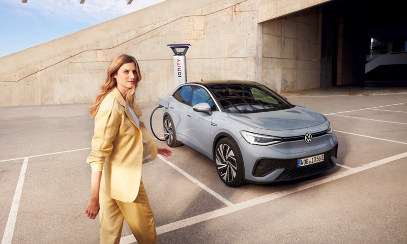 La Volkswagen ID.5 in carica presso una stazione di ricarica. Una donna le passa accanto.