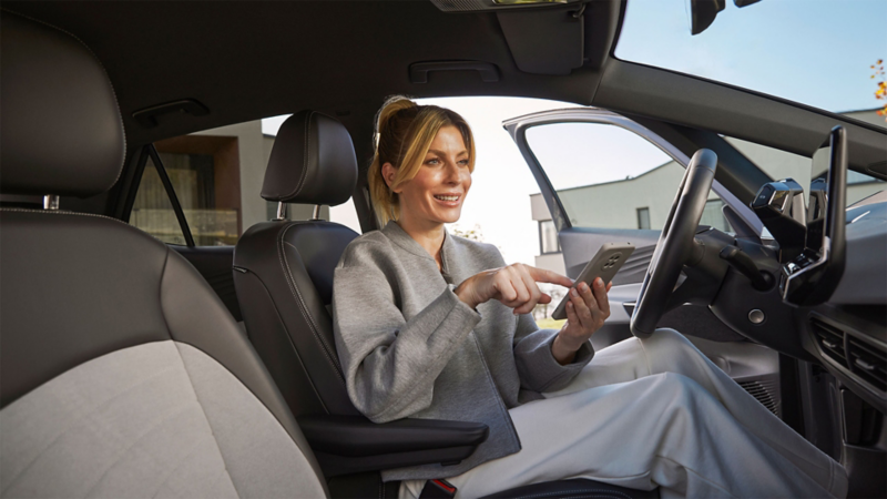 Eine Frau sitzt in einem Volkswagen und tippt auf ihr Handy.