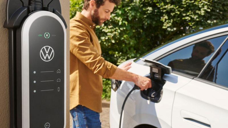 Ein Mann schließt einen weißen VW ID.7 an eine Wallbox an, im Vordergrund ist die Ladestation zu sehen.