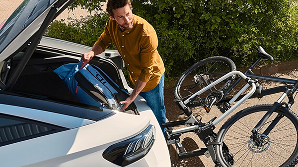 Vista di un uomo caricare nel vano bagagli una valigia e agganciata all'auto una bicicletta.