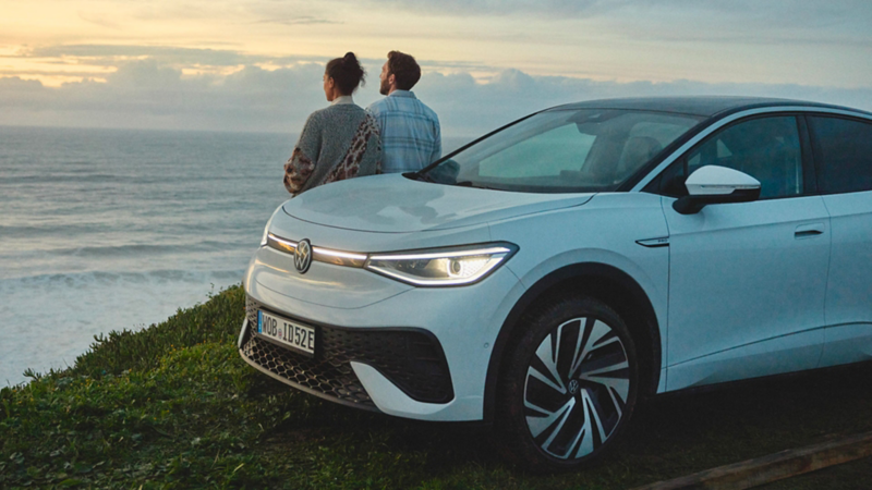 Un uomo e una donna guardano il mare appoggiati a un SUV elettrico Volkswagen.