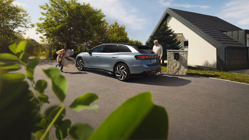 En mann kobler til ladekabelen på vw id7 tourer. Et barn løper forbi
