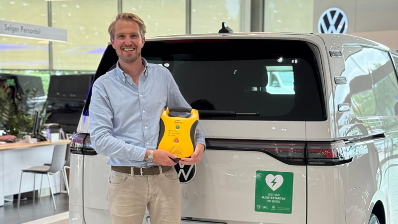 En person står foran en vw varebil og holder en hjertestarter fra lhl