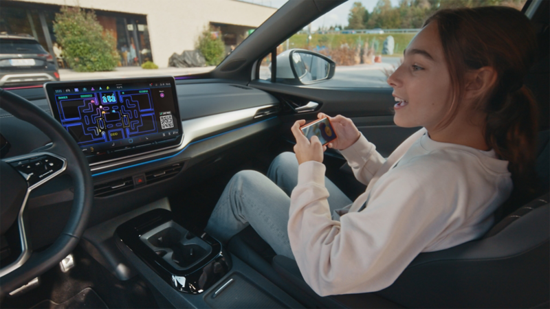 Et barn sitter i passasjersetet i en vw og spiller airconsole med smarttelefonen