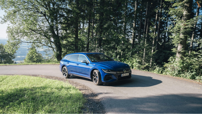 a blue Arteon driving along a tree lined road