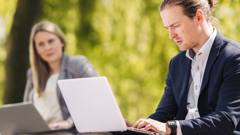 Eine Mitarbeiterin und ein Mitarbeiter von VW arbeiten im Freien an ihren Laptops