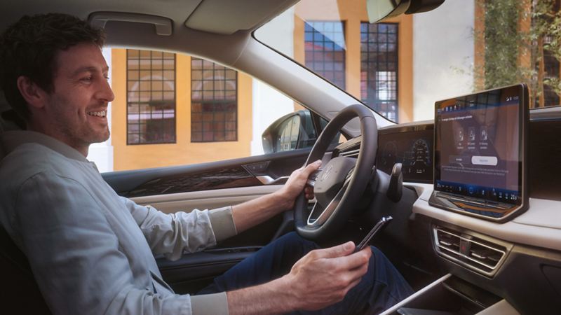 Foto van het interieur van een VW Tiguan. Een man op de bestuurdersstoel bedient met zijn smartphone de optionele VW Connect Plus-applicatie.