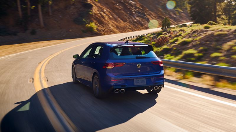 A blue Golf R drives along a two-lane highway