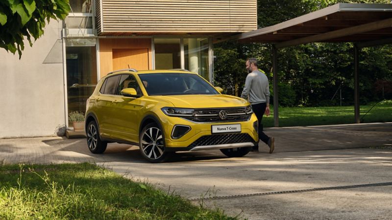 Un uomo sta per salire su una VW T-Cross gialla parcheggiata davanti all'ingresso del giardino di una casa.