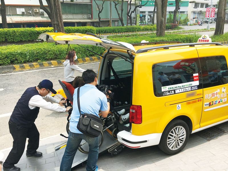 黃色Caddy IPC無障礙計程車，司機下車協助將坐在輪椅上的繞境民眾從後尾門推上車