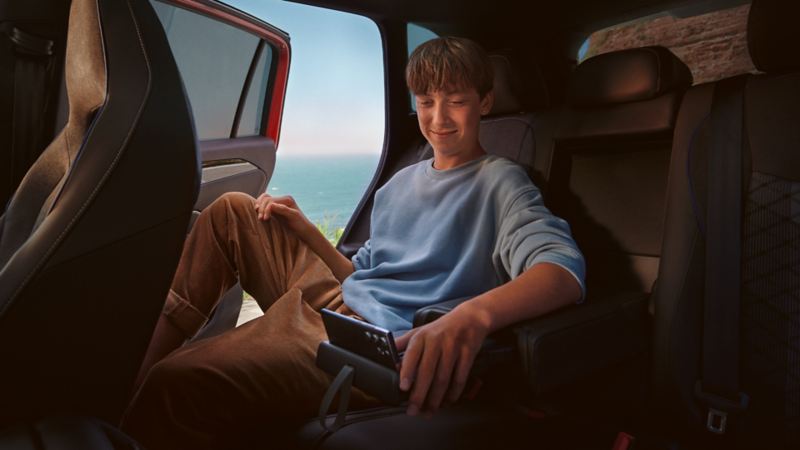 Innenansicht auf die Rückbank des VW Tiguan, wo ein Teenanger auf seinem Tablet, abgestellt auf der Halterung der Mittelkonsole, navigiert. 
