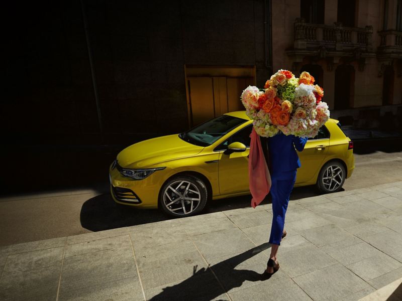 Kvinna med blommor i famnen går framför Volkswagen Nya Golf