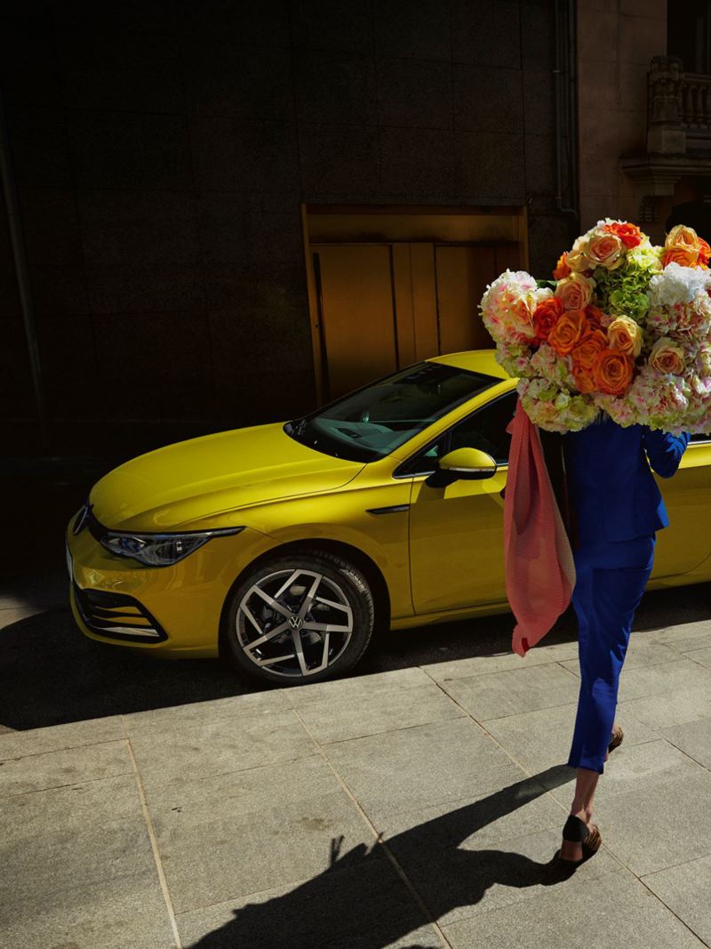 Kvinna med blommor i famnen går framför Volkswagen Nya Golf