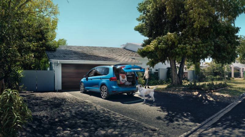 Volkswagen Touran azul aparcado frente a una casa con el portón trasero abierto
