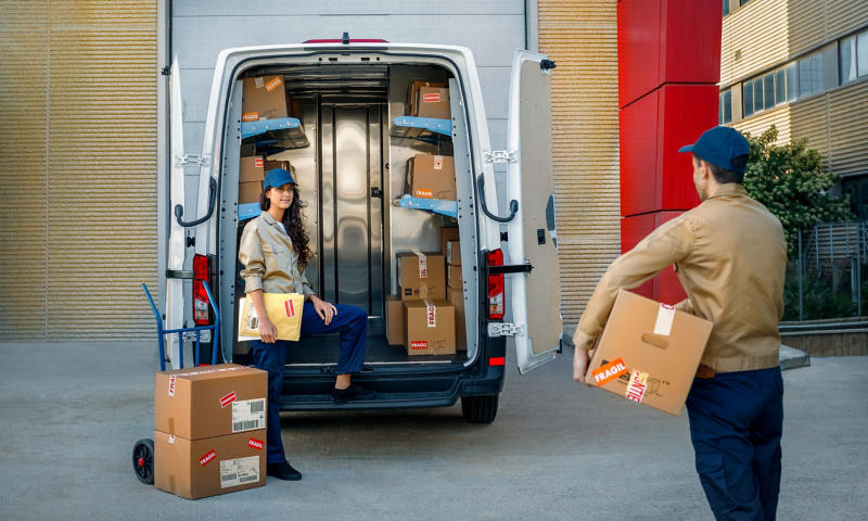 Una pareja de trabajadores junto a la parte trasera del VW Crafter Carrier con paquetes en las baldas abatibles