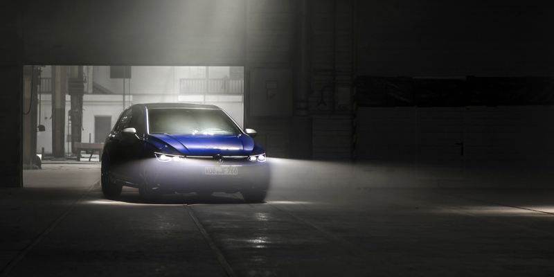 Los faros de un VW Golf R azul iluminan una oscura nave industrial