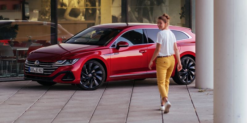 Une femme se tient à côté d'une VW Arteon Shooting Brake rouge