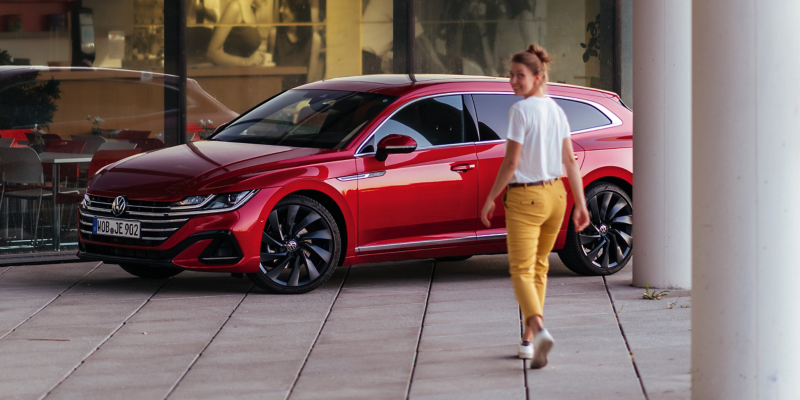 Woman stands next to a red VW Arteon Shooting Brake. VW Accessories