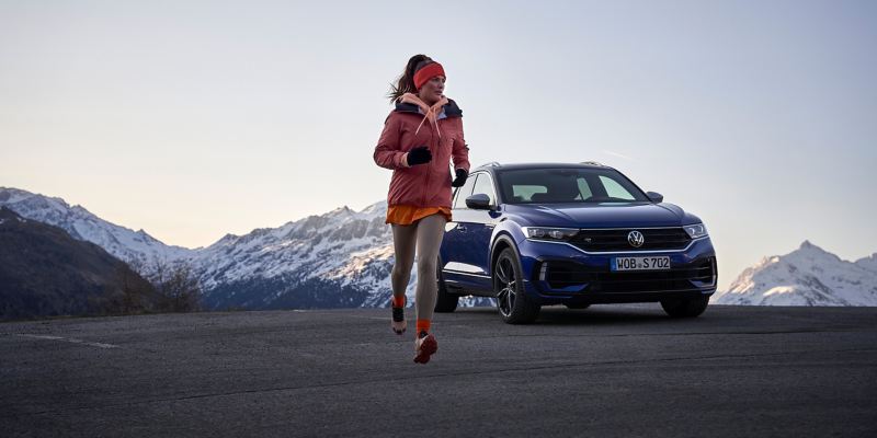 Ein VW T-Roc parkt in einer bergigen Landschaft, eine Frau joggt