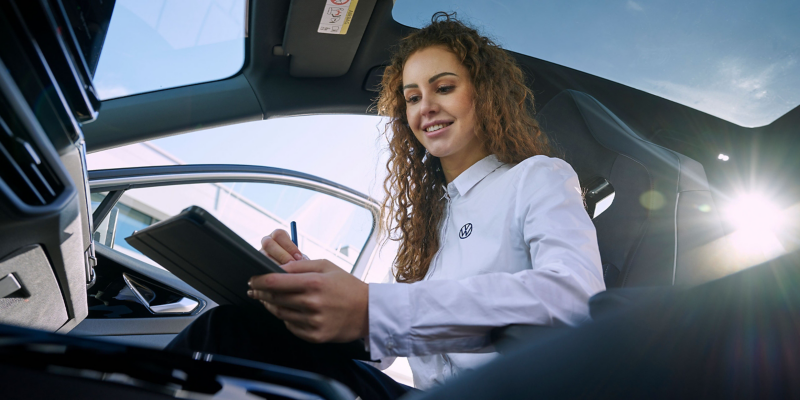 Une collaboratrice du service VW tenant une tablette est assise sur le siège passager d’une voiture VW