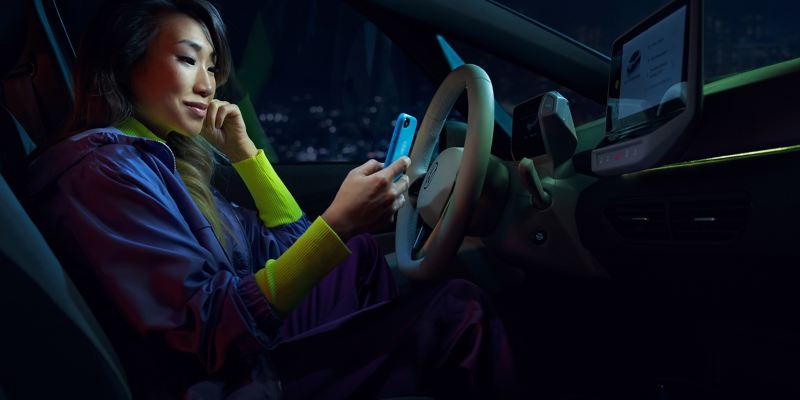 Kobieta siedzi w swoim VW ID.3 i podłącza smartfon do samochodu przez App Connect.