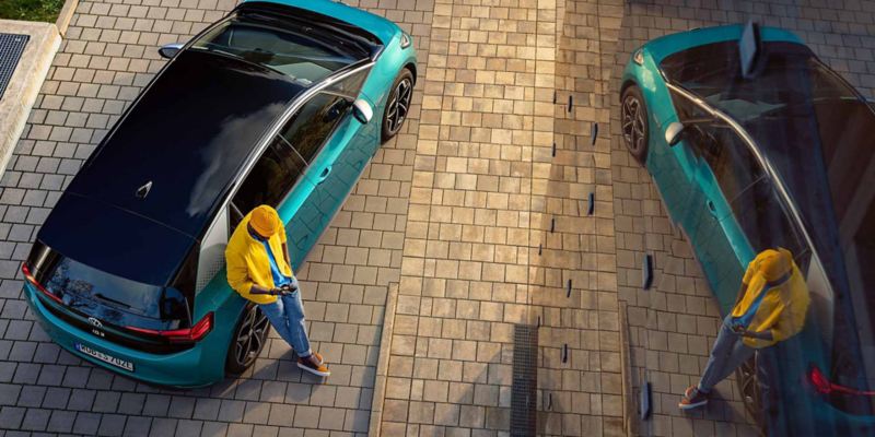 Vista dall'alto un ragazzo appoggiato a un'automobile Volkswagen mentre guarda il suo telefonino.