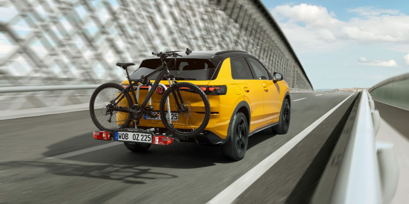 The VW T-Roc with the VW Accessories bicycle carrier and a mounted bicycle driving along a road