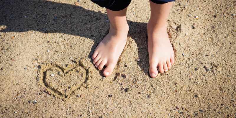 Мальчик босиком стоит на пляже, на песке нарисовано сердце