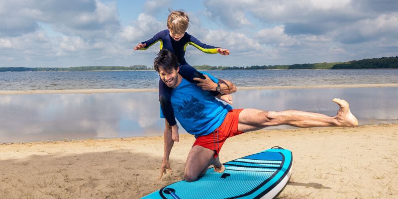 Vater und Sohn stehen auf einem Stand-Up-Paddle Board und albern herum