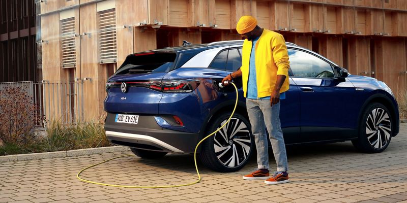 Un homme avec une casquette jaune recharge son ID.4 avec un câble de recharge des Accessoires Volkswagen