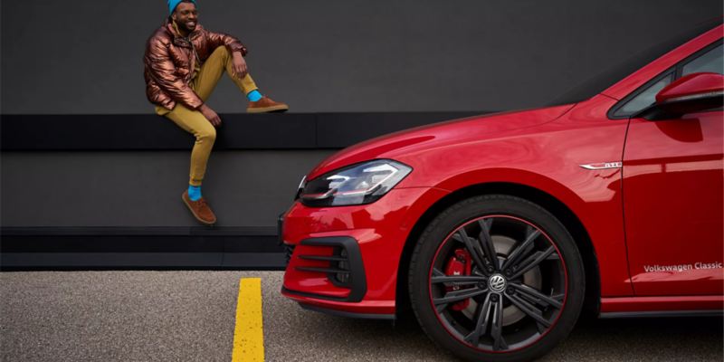 Un hombre elegante admirando el vehículo Volkswagen rojo.