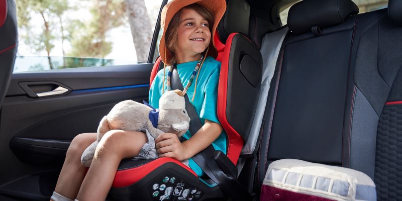 Ein Kind sitzt mit einem Plüschtier auf dem Kindersitz „Kidfix“ im GTI Design – Volkswagen Zubehör