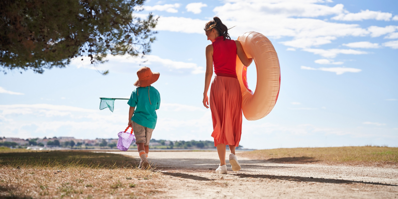 Frau und Kind, mit Spielsachen für den Strand ausgestattet, gehen spazieren