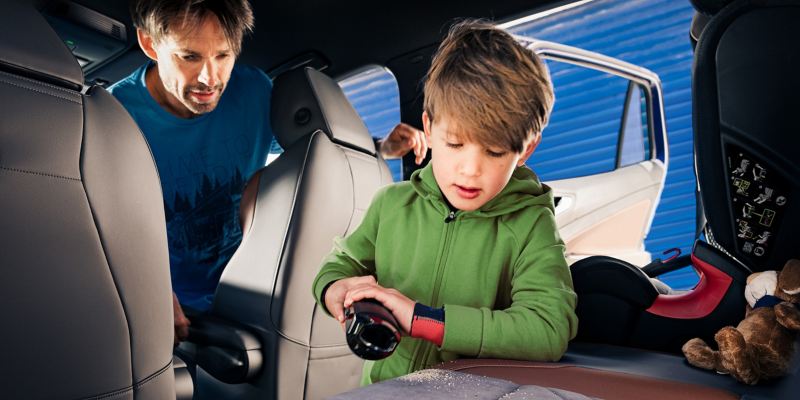 Un bambino gioca sui sedili posteriori di un'auto Volkswagen mentre il padre lo osserva dai posti anteriori.