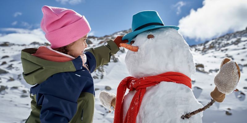 Ein Mädchen baut einen Schneemann mit Hut, Handschuhen und Schal