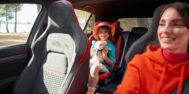 Mutter und Sohn im Auto, Kind sitzt mit Plüschtier auf Kindersitz „Kidfix“ im GTI Design – Volkswagen Zubehör