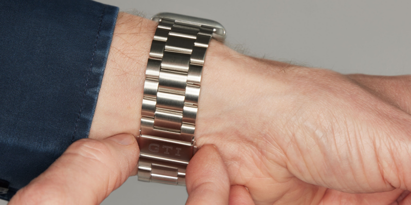 Hombre sujetando con el pulgar y el índice el cierre de mariposa de una correa para smartwatch con el logotipo GTI.