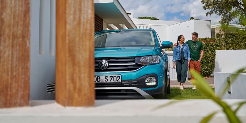 Une VW T-Cross stationnée sur une propriété, un couple marche à côté du véhicule