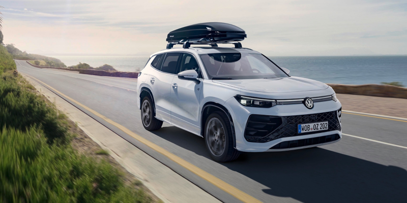 Un Volkswagen Tayron R-Line con baúl de techo circulando por una carretera, con el mar al fondo