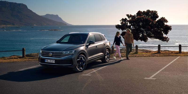 Un homme et une femme à côté d’une VW Touareg, l’océan en arrière-plan