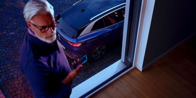 Hombre con un móvil junto a una ventana y un Volkswagen ID.4 detrás