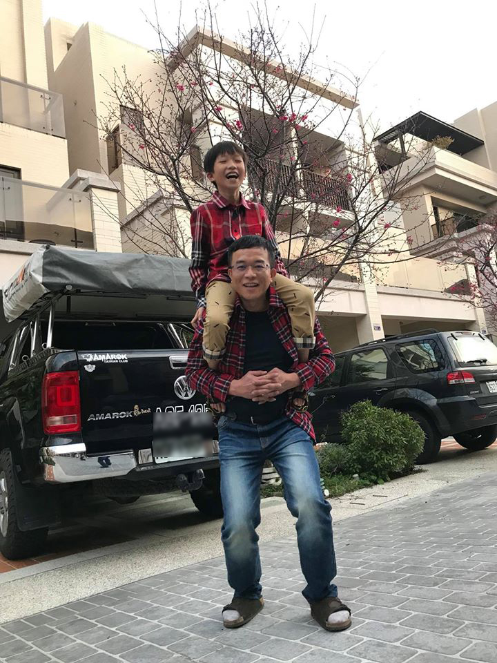 小男孩坐在爸爸車主肩膀上、站在黑色Amarok車尾前拍照