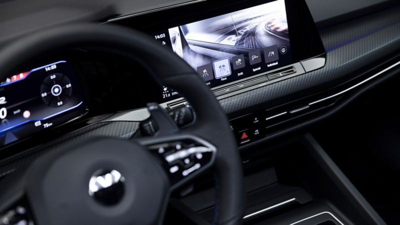 Plan rapproché du volant de la toute nouvelle Golf R 2022. Derrière celui-ci, on aperçoit le cockpit numérique à écran tactile affichant les divers modes de conduite.
